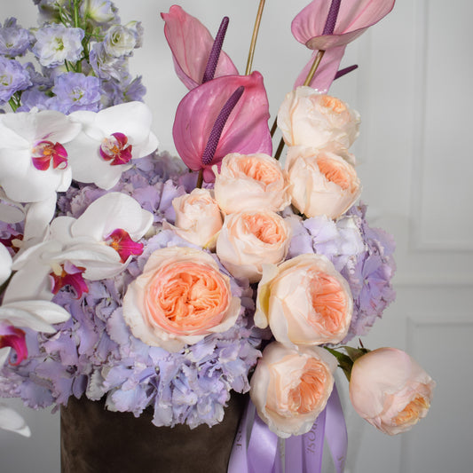 Close-up of peach David Austin roses, lilac hydrangeas and pink anthuriums in AMEROSE Lavender Dream hatbox