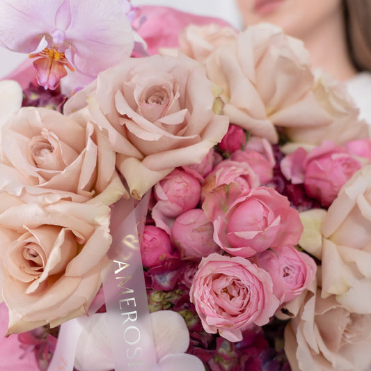 Close-up of dusty mocha roses, hot pink spray roses, lavender phalaenopsis orchid and burgundy hydrangeas with AMEROSE gold ribbon — luxury textured bouquet detail London