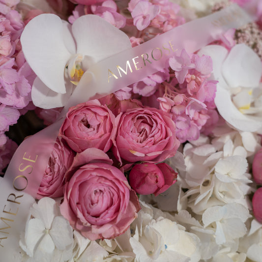 Close-up of pink spray roses, white phalaenopsis orchids, pink and white hydrangeas with AMEROSE gold ribbon — luxury hatbox flower arrangement detail London