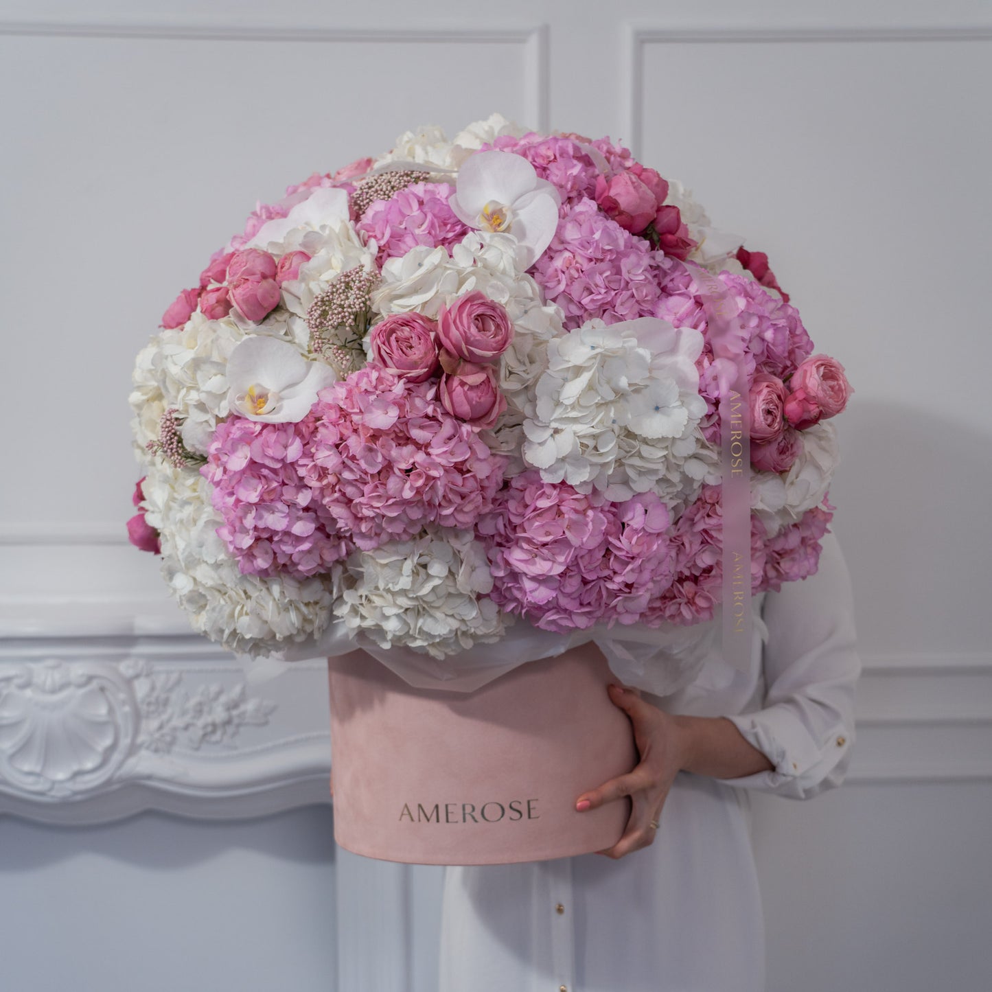 Person holding an oversized AMEROSE blush velvet hatbox completely filled with a massive cloud of pink and white hydrangeas, spray roses and orchids — statement luxury flowers London