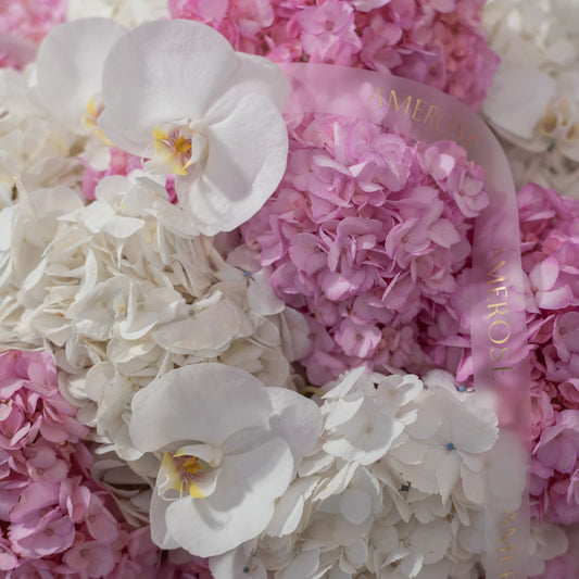 Close-up of white phalaenopsis orchids nestled among pink and white hydrangeas with AMEROSE sheer gold ribbon — luxury flower arrangement detail London