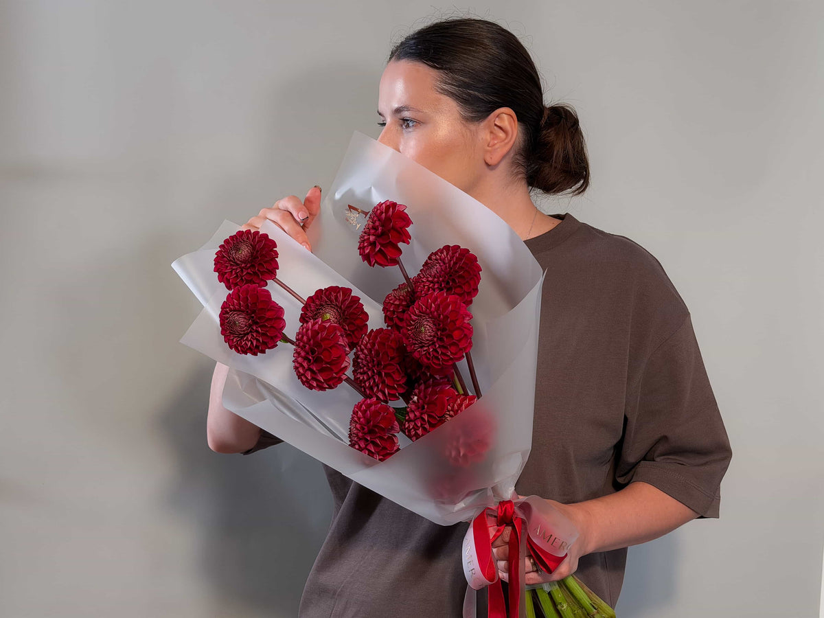 Woman holding a bouquet of red dahlias by AMEROSE against a grey wall