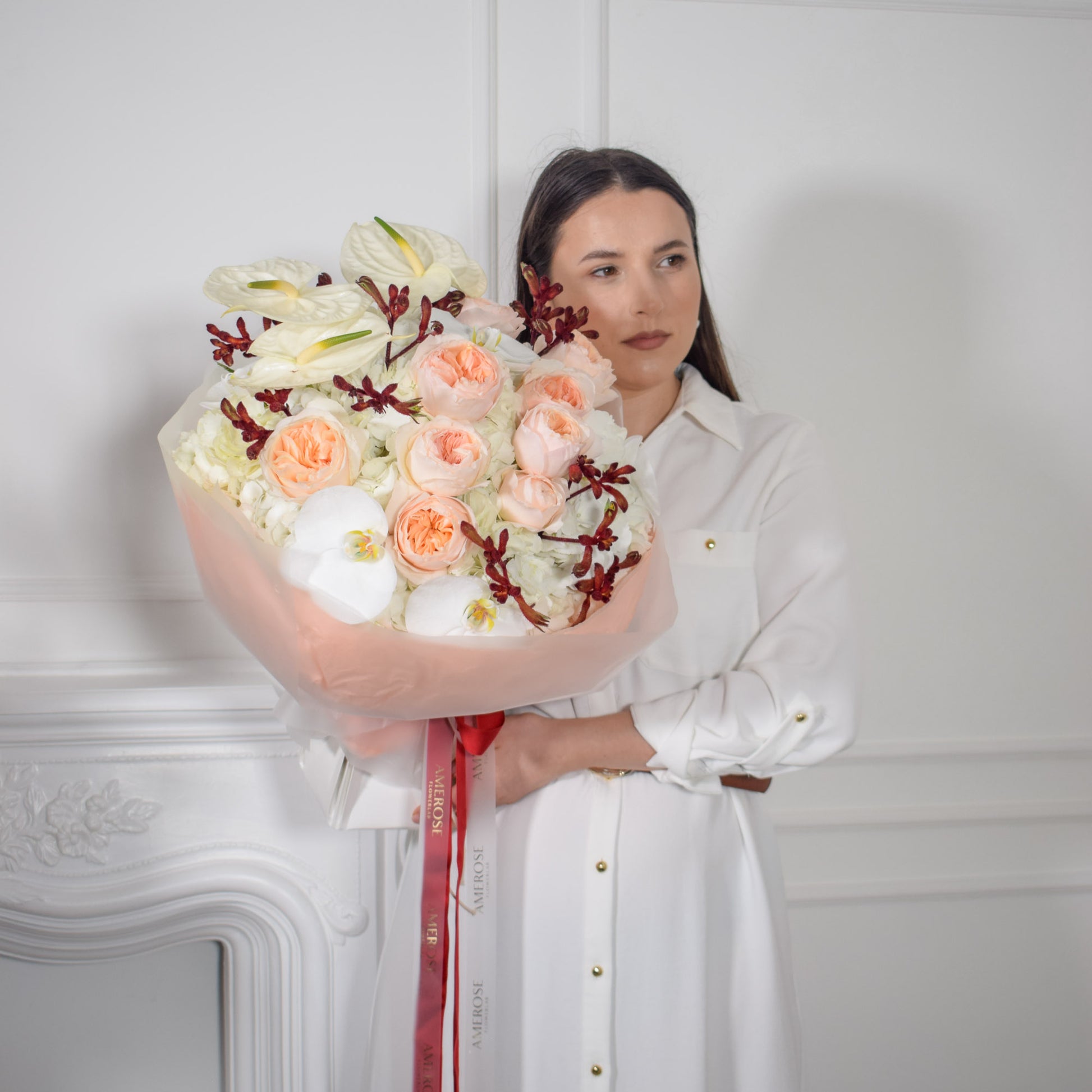 AMEROSE Bordeaux bouquet — Juliet David Austin roses, white orchids and burgundy foliage, held by model in white dress