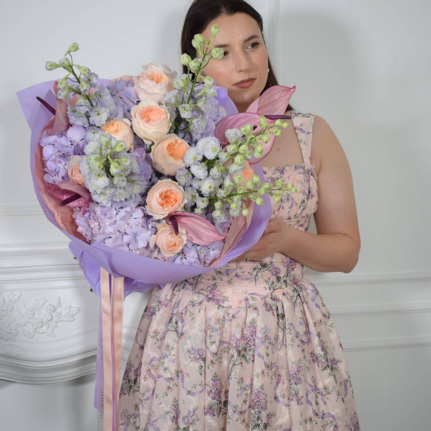 AMEROSE Lilac Dream bouquet — lilac hydrangeas, delphiniums, David Austin roses and pink anthuriums, held by model in floral dress