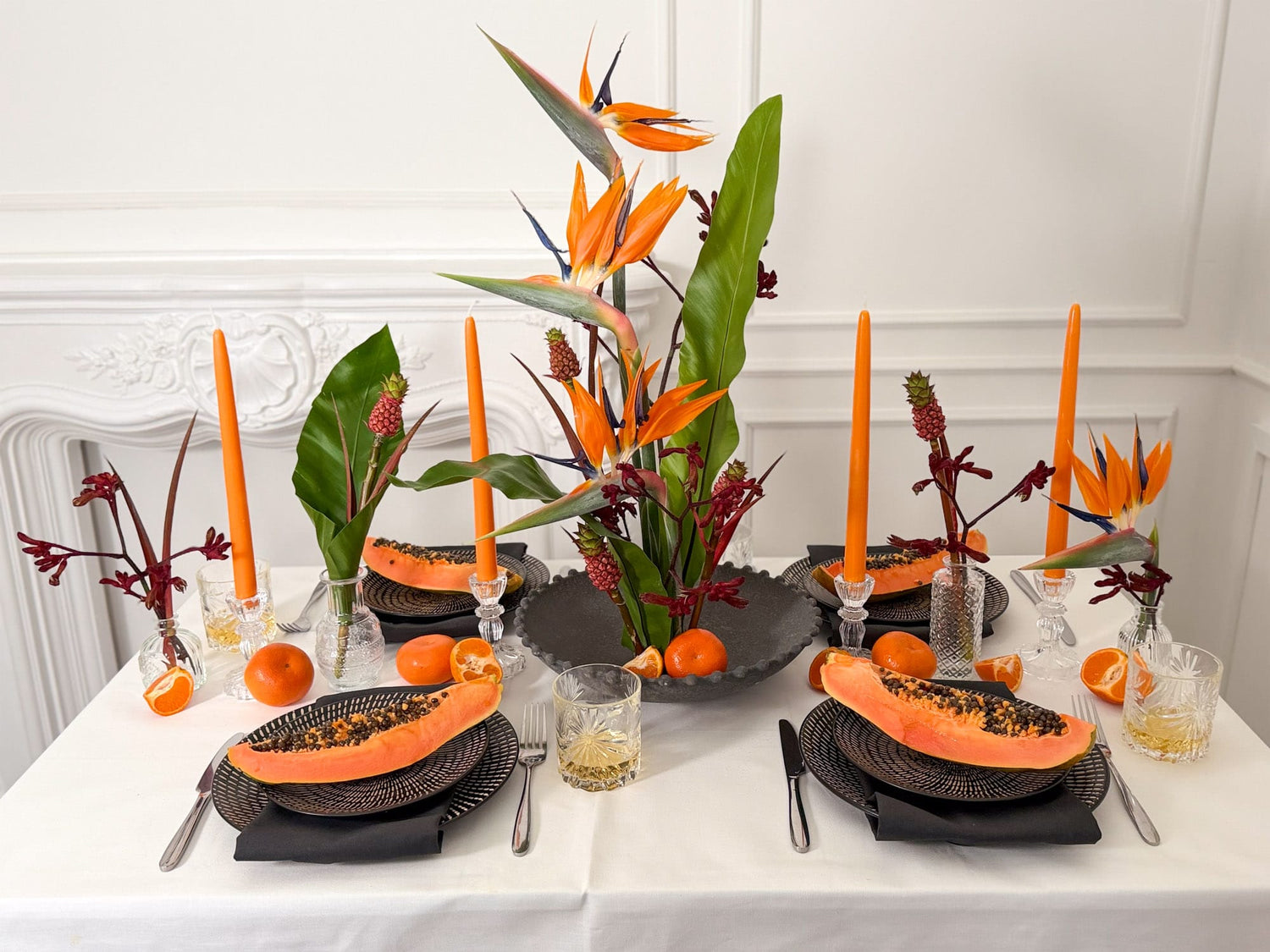Decorative table setting with papaya slices, candles, and tropical flowers by AMEROSE on a white tablecloth for events.