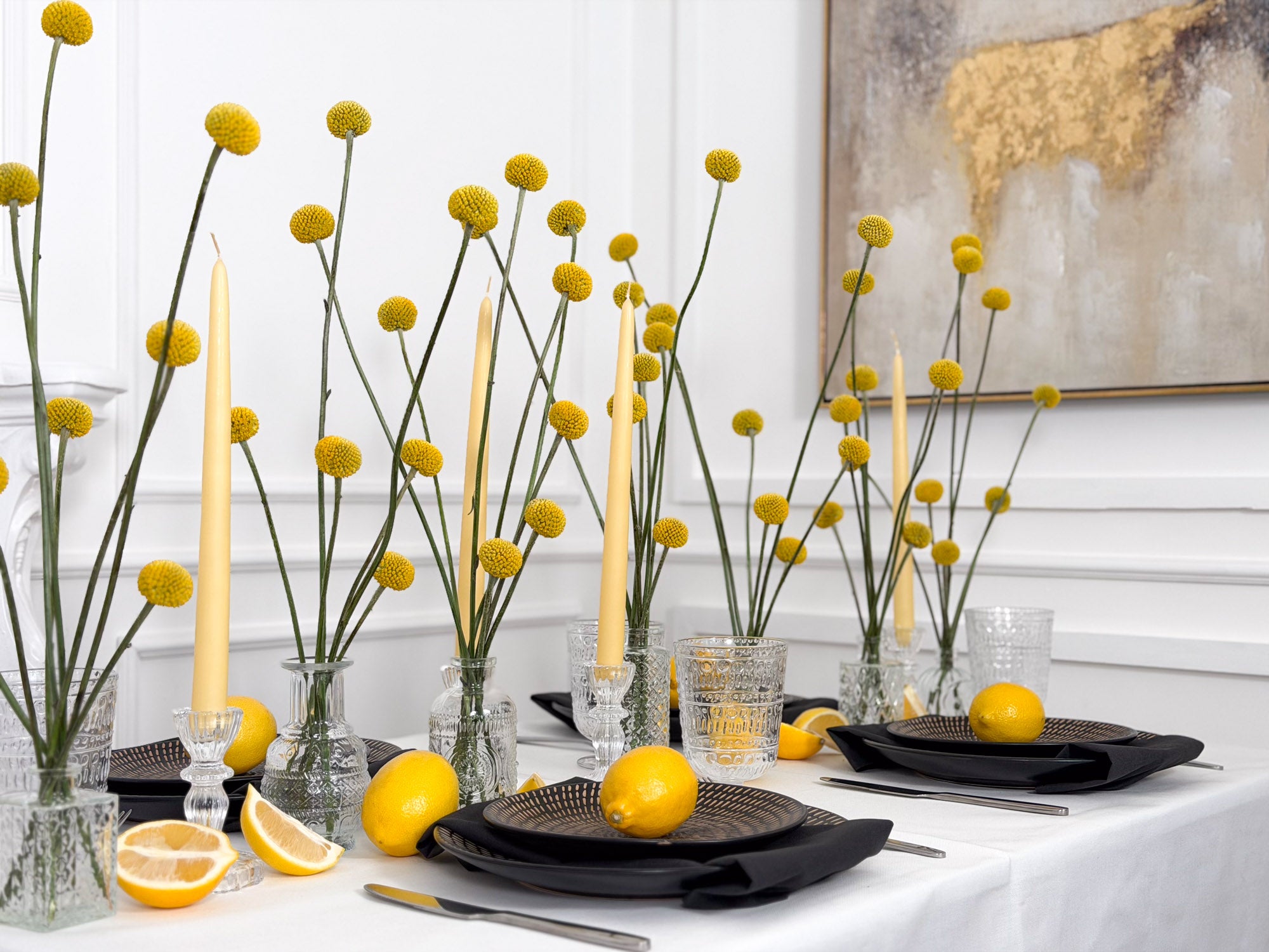 Decorative table setting with yellow flowers, candles, and lemons on a white tablecloth by AMEROSE for events.