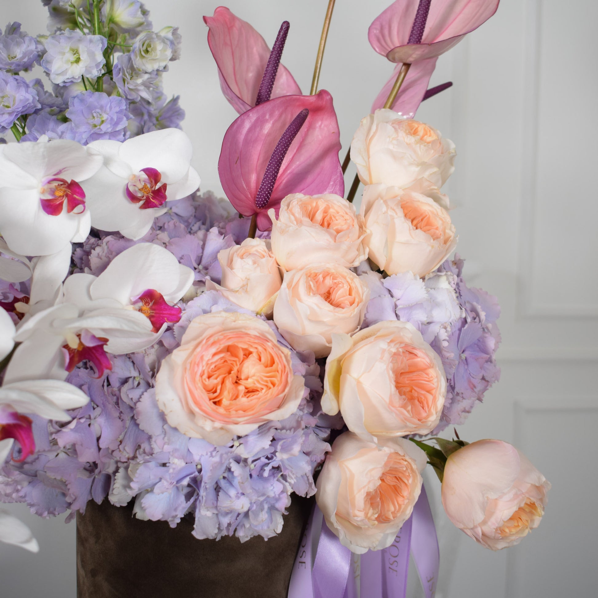 Close-up of peach David Austin roses, lilac hydrangeas and pink anthuriums in AMEROSE Lavender Dream hatbox