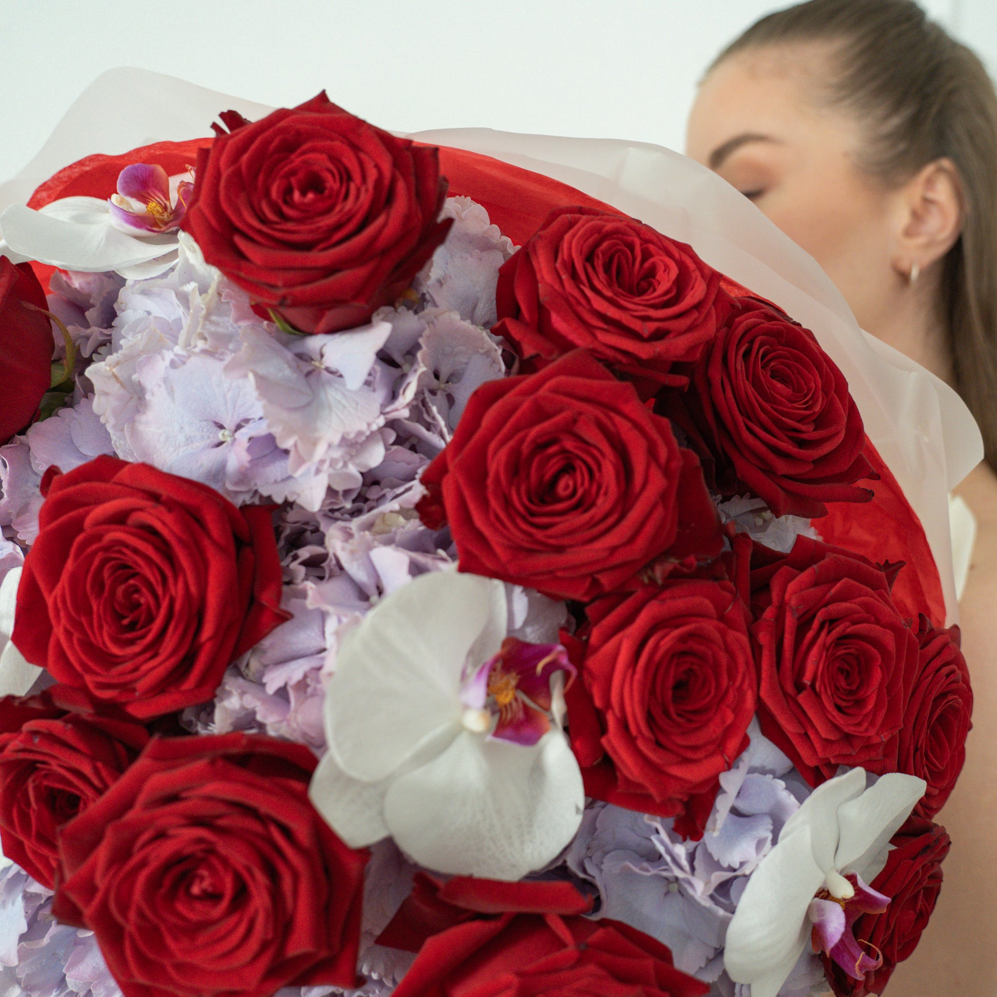 Close-up of deep red roses, lilac hydrangeas and white phalaenopsis orchids in AMEROSE Red Velvet Garden bouquet