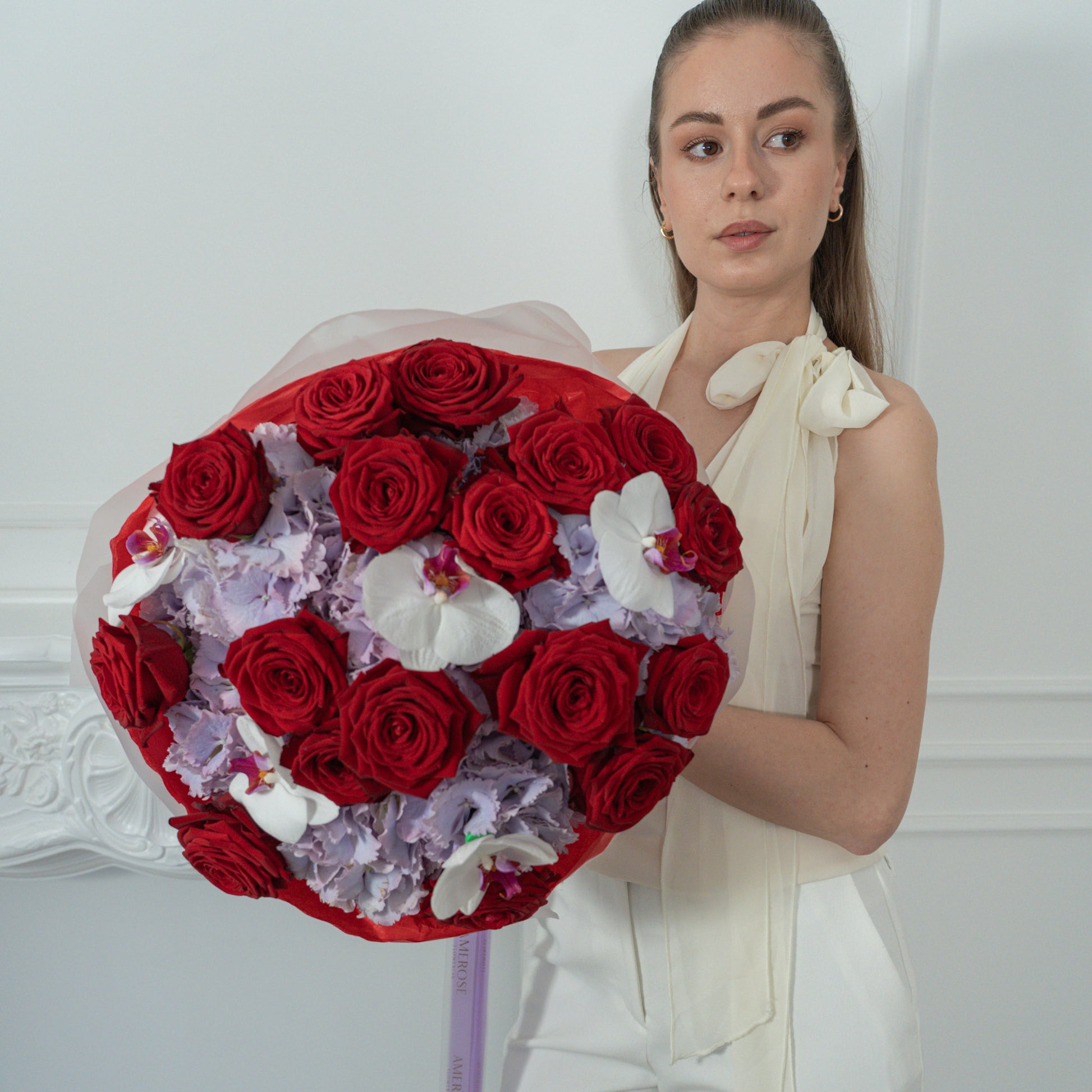 AMEROSE Red Velvet Garden bouquet — deep red roses, lilac hydrangeas and white orchids, held by model in white dress