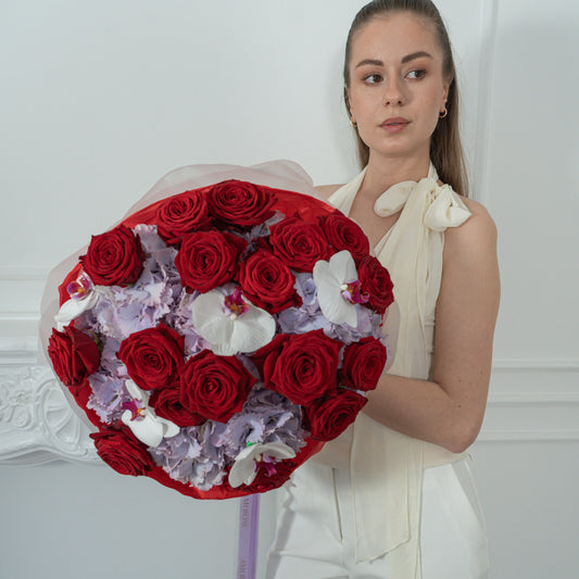 AMEROSE Red Velvet Garden bouquet — deep red roses, lilac hydrangeas and white orchids, held by model in white dress