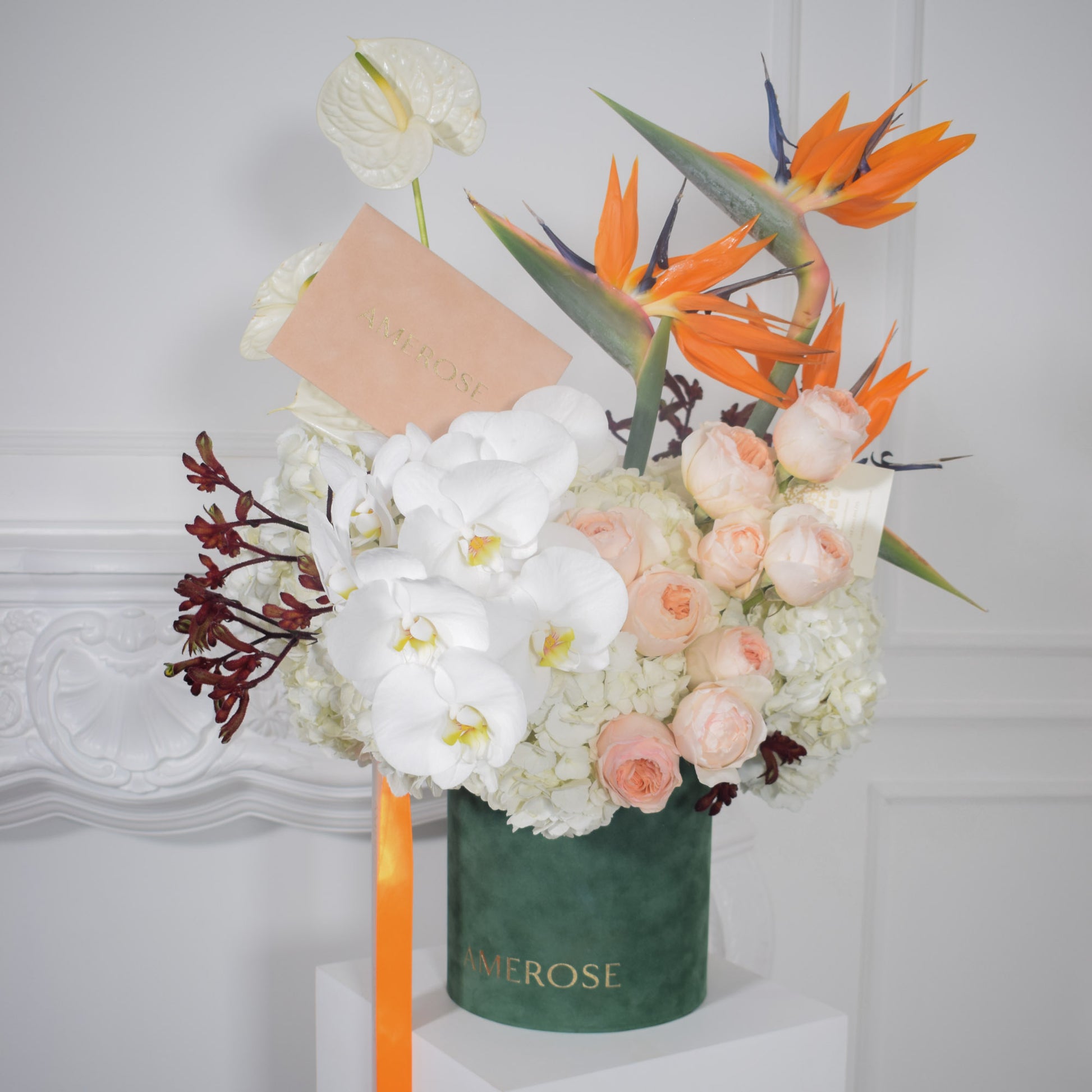 Top view of AMEROSE Birds of Paradise signature hatbox arrangement with orange birds of paradise, white orchids and peach roses