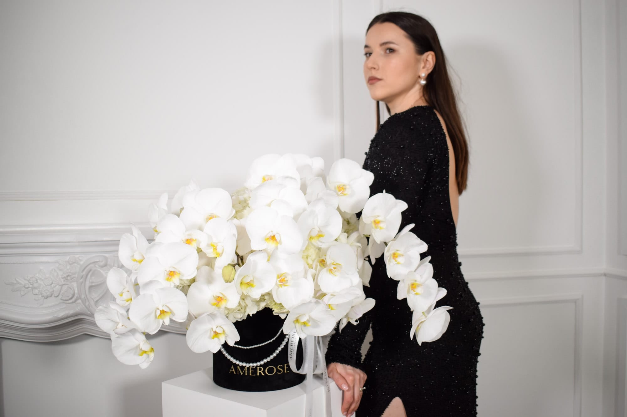 Woman in a black dress standing next to a large arrangement of hydrangeas and orchids by AMEROSE