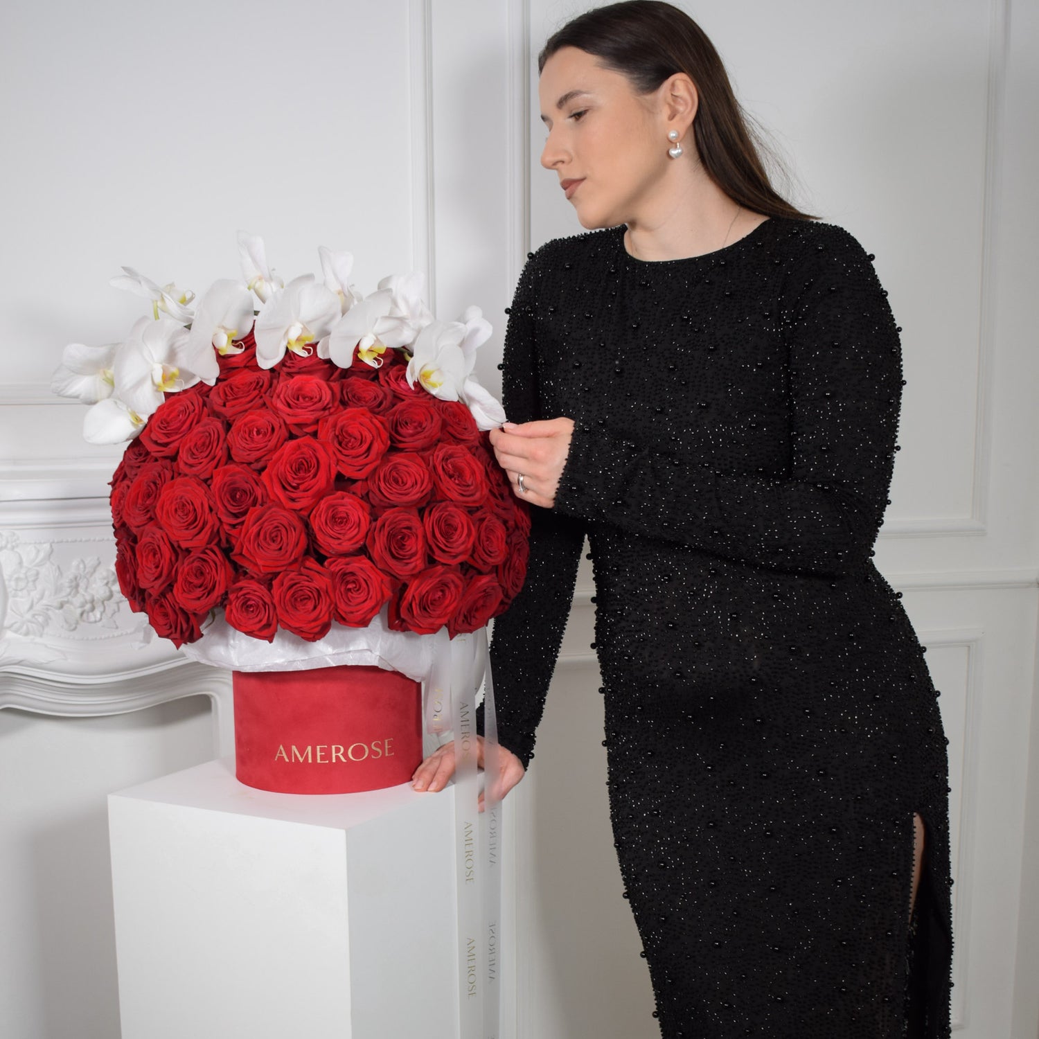 AMEROSE Rouge signature hatbox — 100 deep red roses and white orchids in scarlet velvet hatbox, held by model in black dress