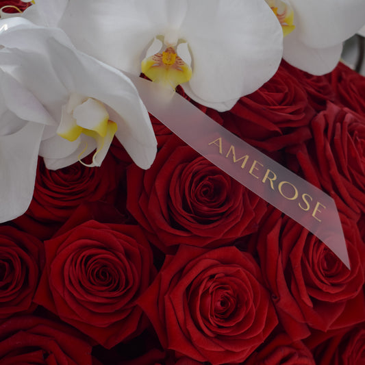 Close-up of deep red roses with AMEROSE signature satin ribbon and white orchids in Rouge luxury hatbox