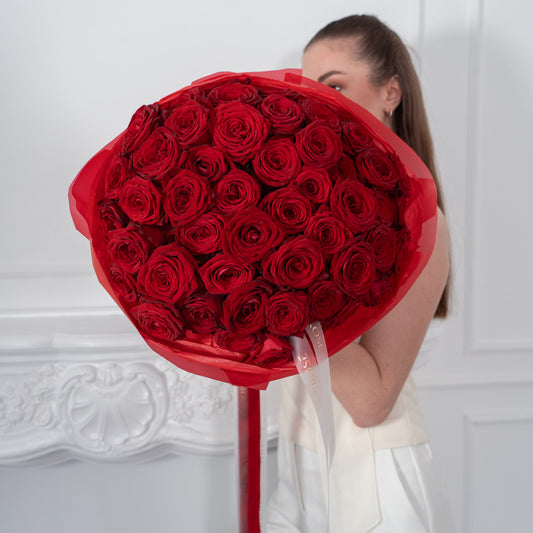 AMEROSE The Classic Roses — perfect dome of deep red roses in signature red tissue, held by model in white dress