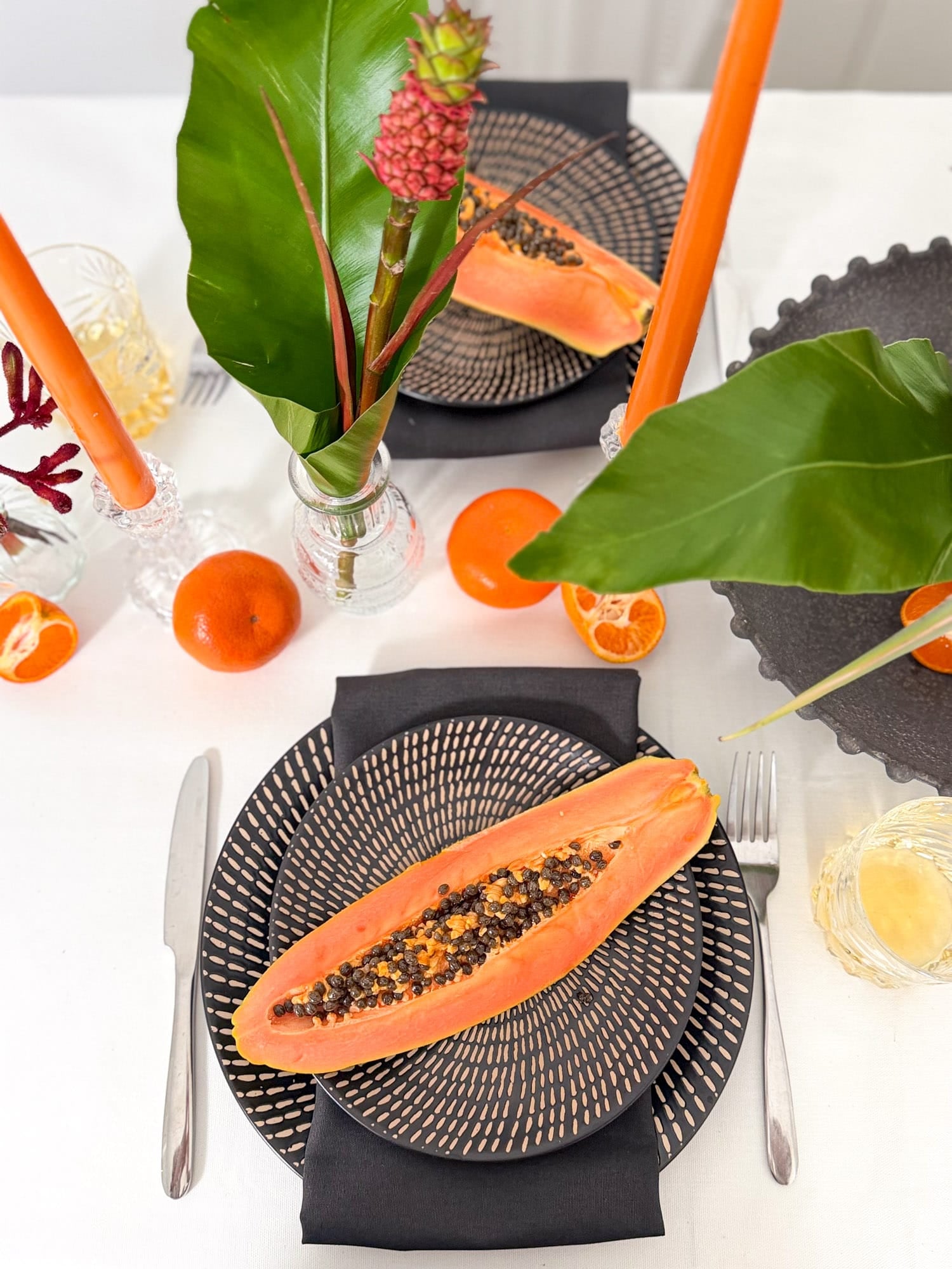 Table setting with a halved papaya on a woven plate, surrounded by tropical decor by AMEROSE.
