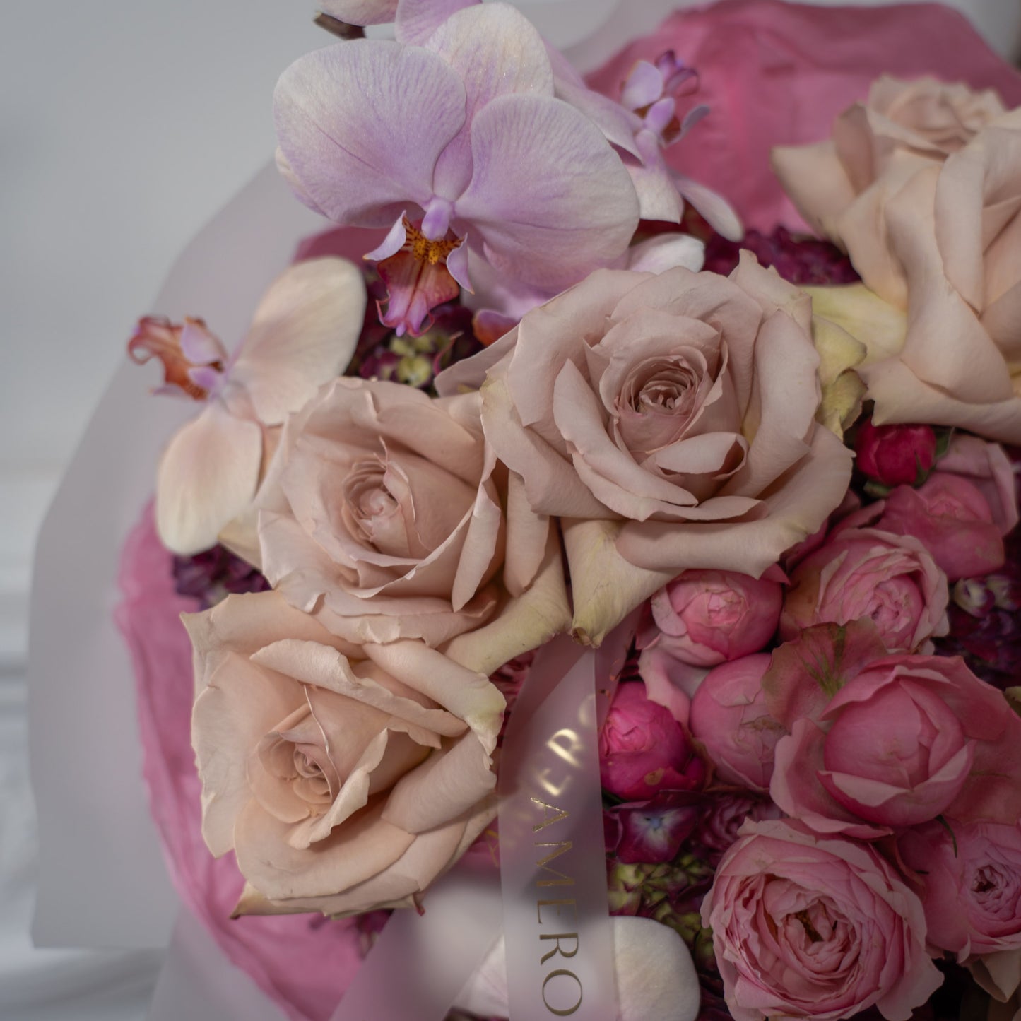 Close-up of dusty mocha roses, hot pink spray roses, lavender phalaenopsis orchid and burgundy hydrangeas with AMEROSE gold ribbon — luxury textured bouquet detail London