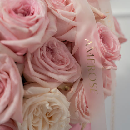 Close-up of blush pink and cream O'Hara garden roses with ruffled petals and AMEROSE gold satin ribbon — luxury rose hatbox detail London