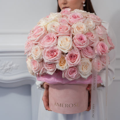 Woman holding an oversized AMEROSE blush velvet hatbox filled with a dome of pink and cream O'Hara garden roses — premium flower delivery London