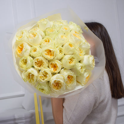 Bouquet of butter yellow garden roses by AMEROSE held by a person against a white background