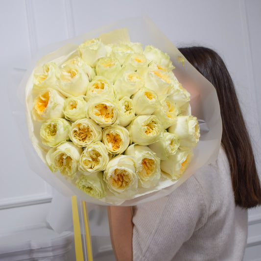 Bouquet of butter yellow garden roses by AMEROSE held by a person against a white background