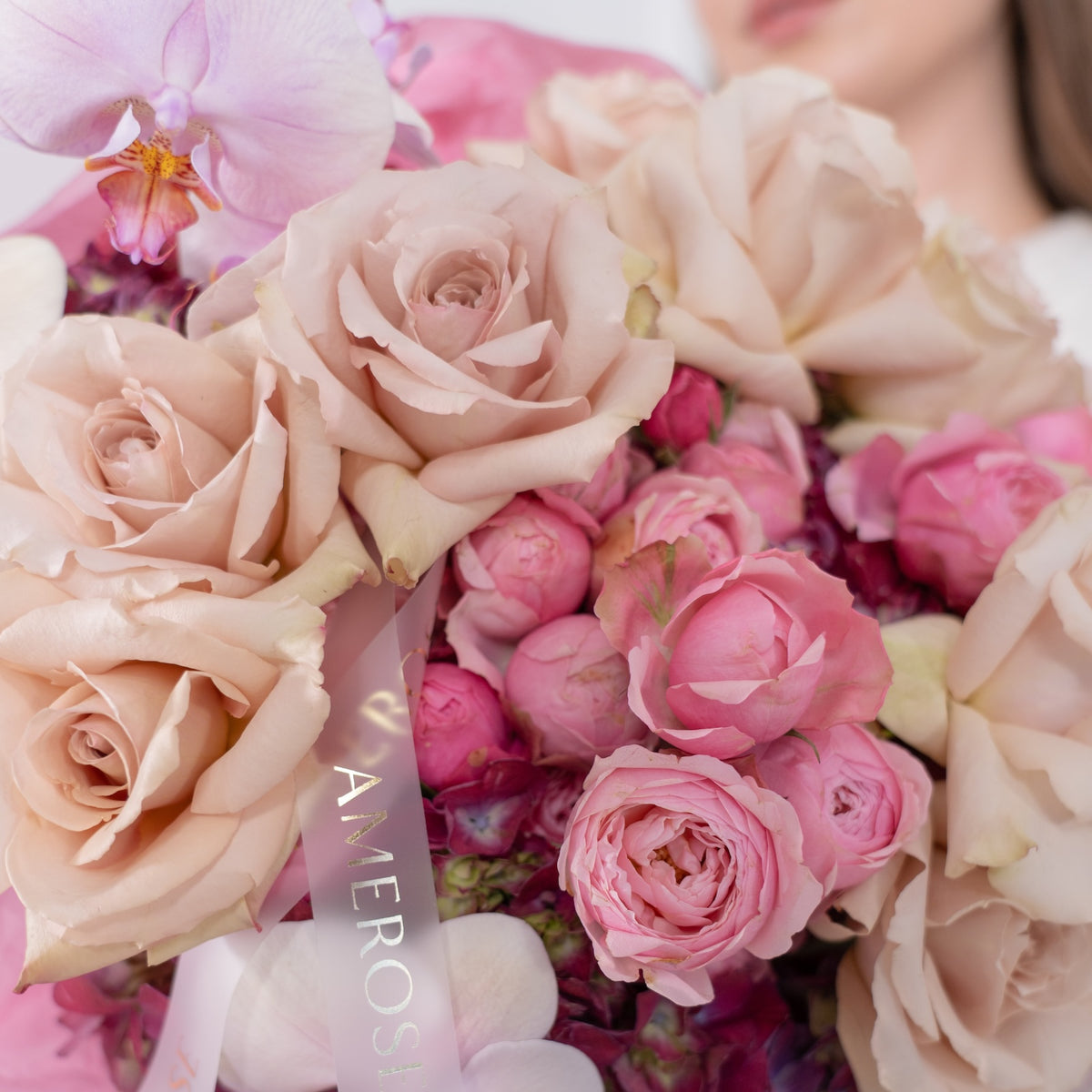 Close-up of dusty mocha roses, hot pink spray roses, lavender phalaenopsis orchid and burgundy hydrangeas with AMEROSE gold ribbon — luxury textured bouquet detail London