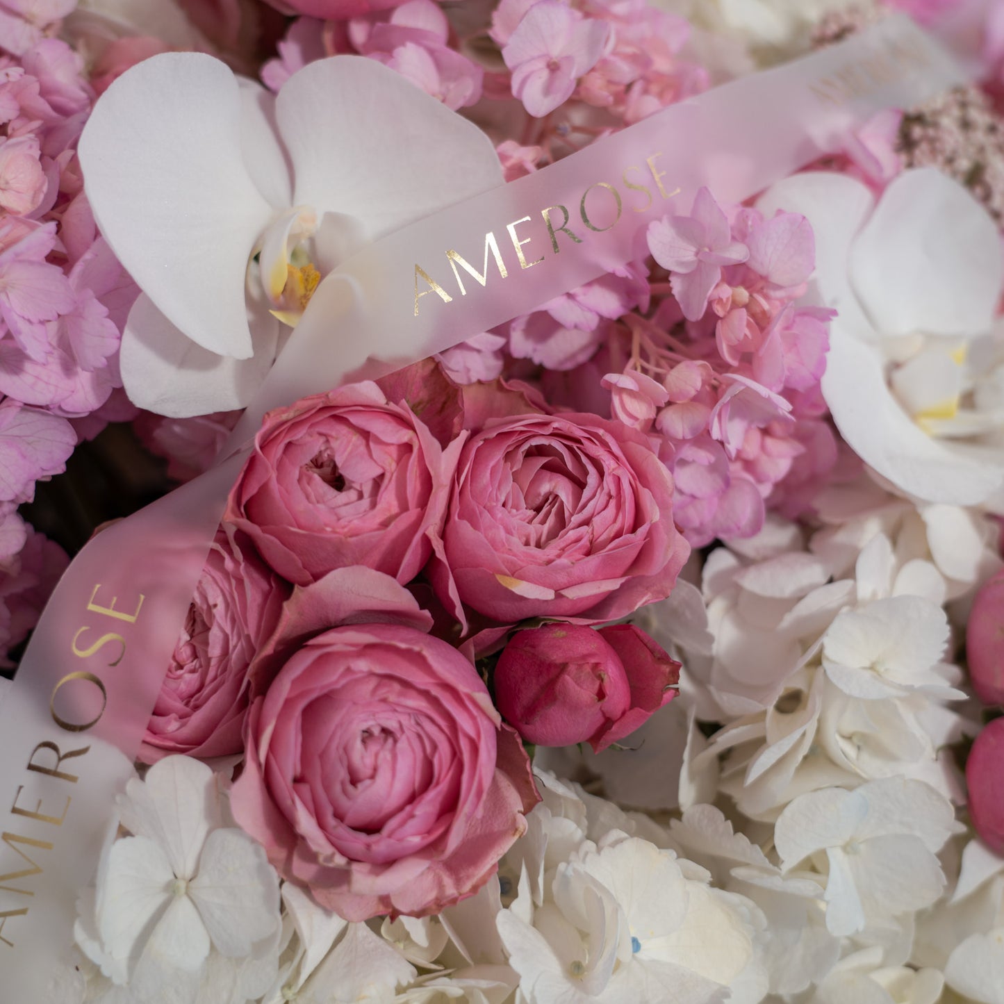 Close-up of pink spray roses, white phalaenopsis orchids, pink and white hydrangeas with AMEROSE gold ribbon — luxury hatbox flower arrangement detail London