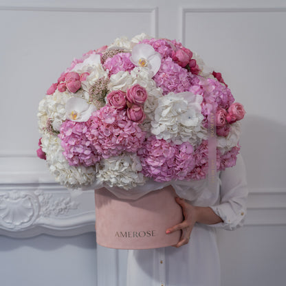Person holding an oversized AMEROSE blush velvet hatbox completely filled with a massive cloud of pink and white hydrangeas, spray roses and orchids — statement luxury flowers London
