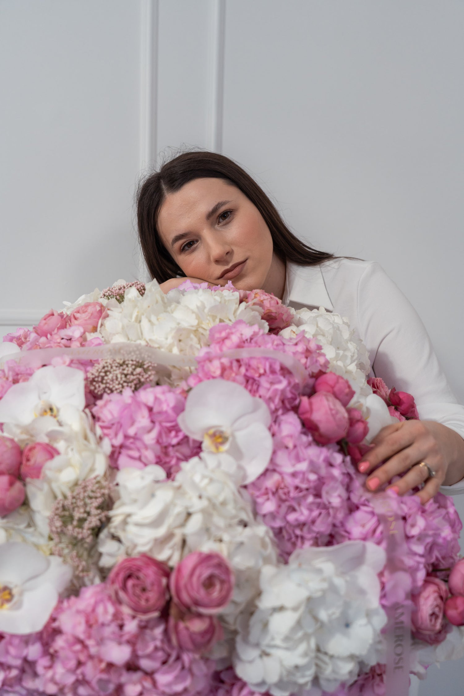 Woman surrounded by a large bouquet of pink and white flowers against a plain background - AMEROSE London