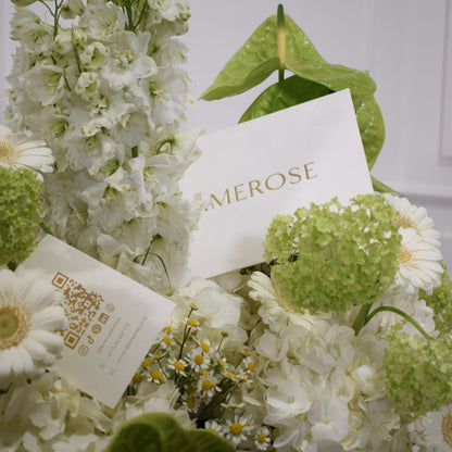 Close-up of green anthurium leaves, white stock, green viburnum, white gerbera daisies and chamomile with AMEROSE branded card — luxury green flower arrangement detail London