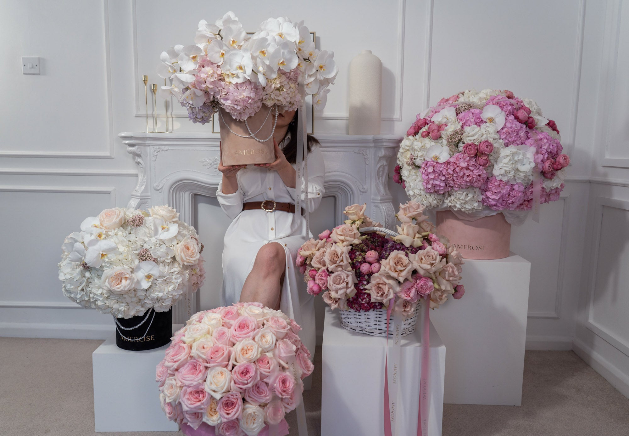 AMEROSE luxury flower arrangements — Orchid Couture hatbox, pink rose hatbox, blush basket displayed in an elegant white interior with model