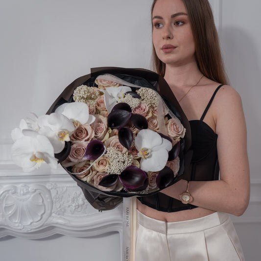 Woman holding a dramatic luxury bouquet of black calla lilies, nude roses and white orchids wrapped in black film with AMEROSE cream ribbon — editorial flower delivery London